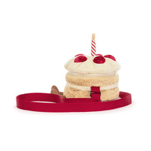 A plush cake-shaped bag with cream-colored frosting, red cherry details, a striped candle, and a red strap, shown on a plain white background. Side view.